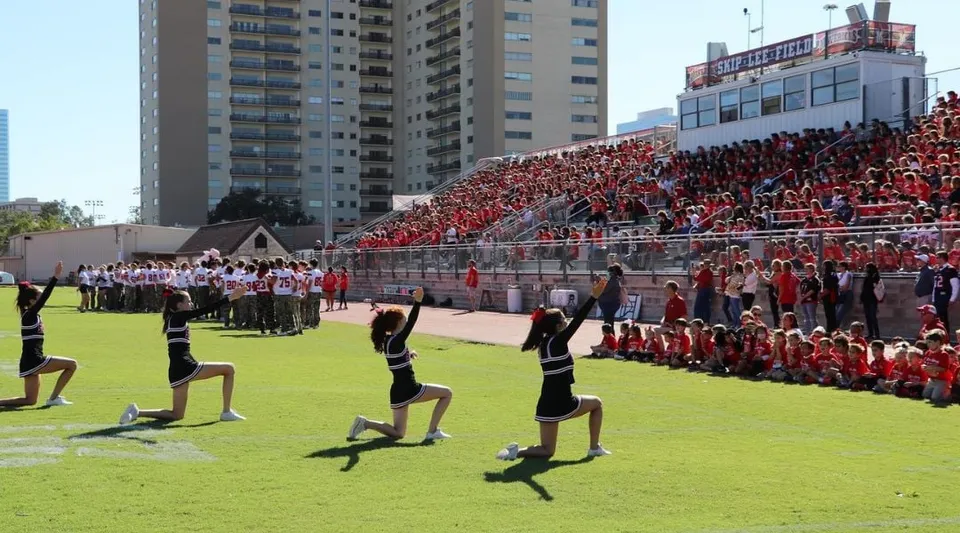 Gli studenti della St. John's School si radunano in divisa rossa e bianca sul campo sportivo davanti ai grattacieli.