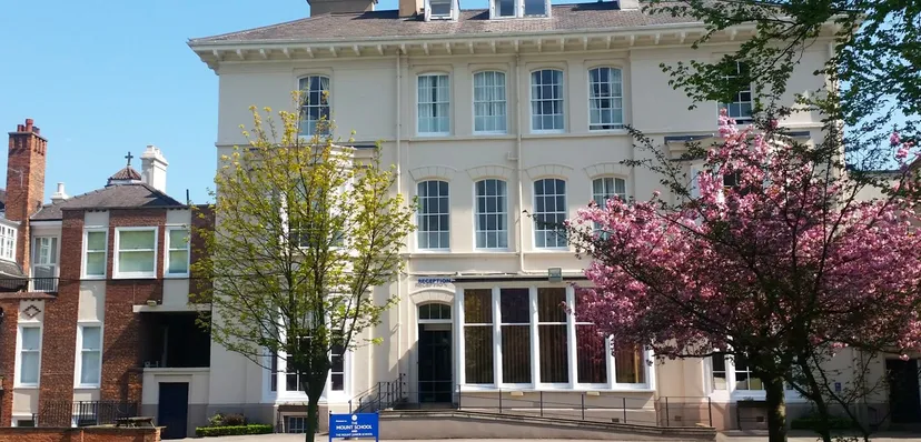 L'edificio a più piani della The Mount School York è circondato da alberi in fiore e da un cielo limpido.