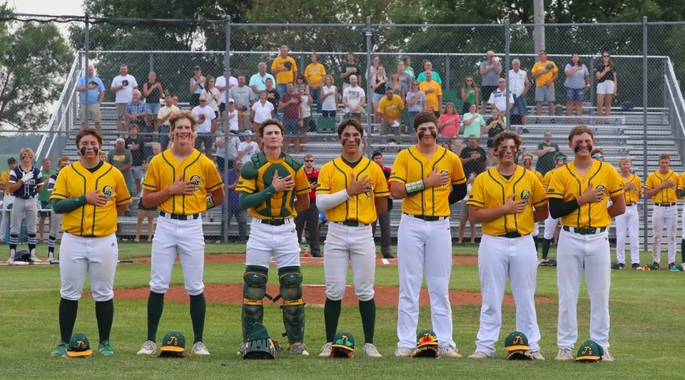 Studenti della Gehlen Catholic School con maglie gialle insieme sul campo da baseball davanti agli spettatori.