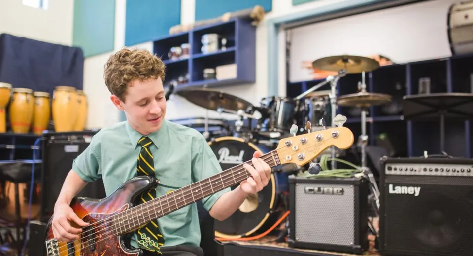 Uno studente del St. Brendan's College suona la chitarra elettrica in uno studio musicale con strumenti musicali sullo sfondo.