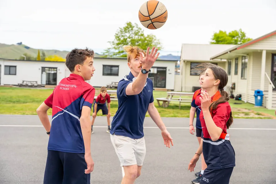 Gli studenti della Richmond View School giocano a pallacanestro con un insegnante nel cortile della scuola.