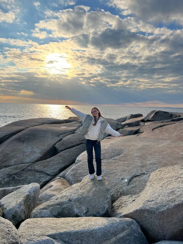 Chica con los brazos abiertos sobre rocas de granito junto al mar al atardecer