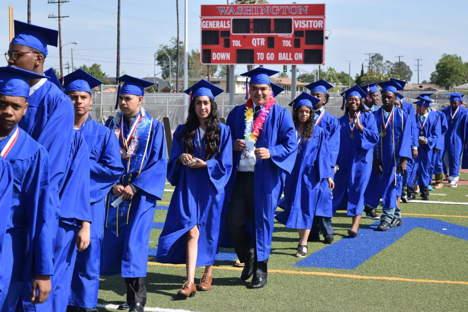 I diplomati della Washington Preparatory School sono in toga sul campo sportivo, con il tabellone visibile.