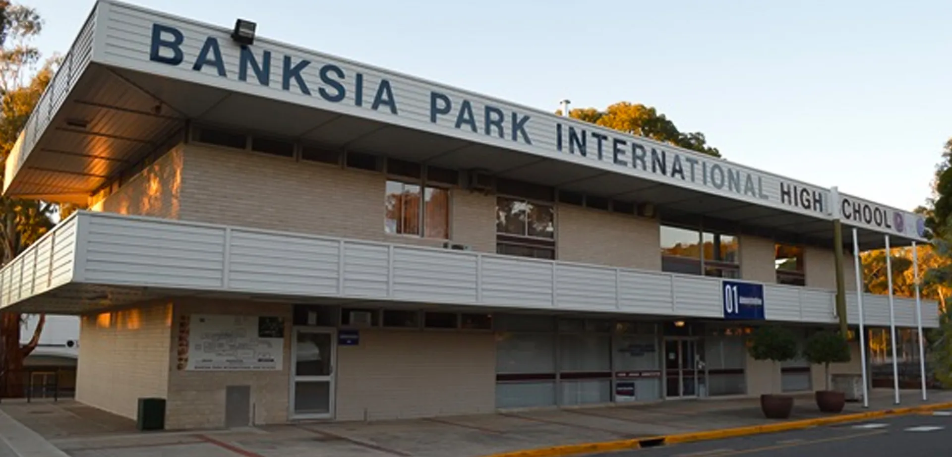 L'ingresso della Banksia Park International High School con un cartello ben visibile davanti ad alberi e cielo blu.