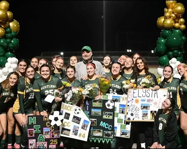 Equipo femenino de fútbol celebrando con flores y carteles caseros en el campo iluminado