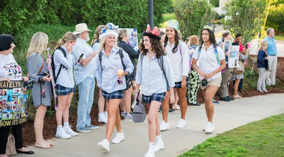 Un gruppo di studentesse della Mount De Sales Academy cammina insieme lungo un sentiero circondato da alberi.