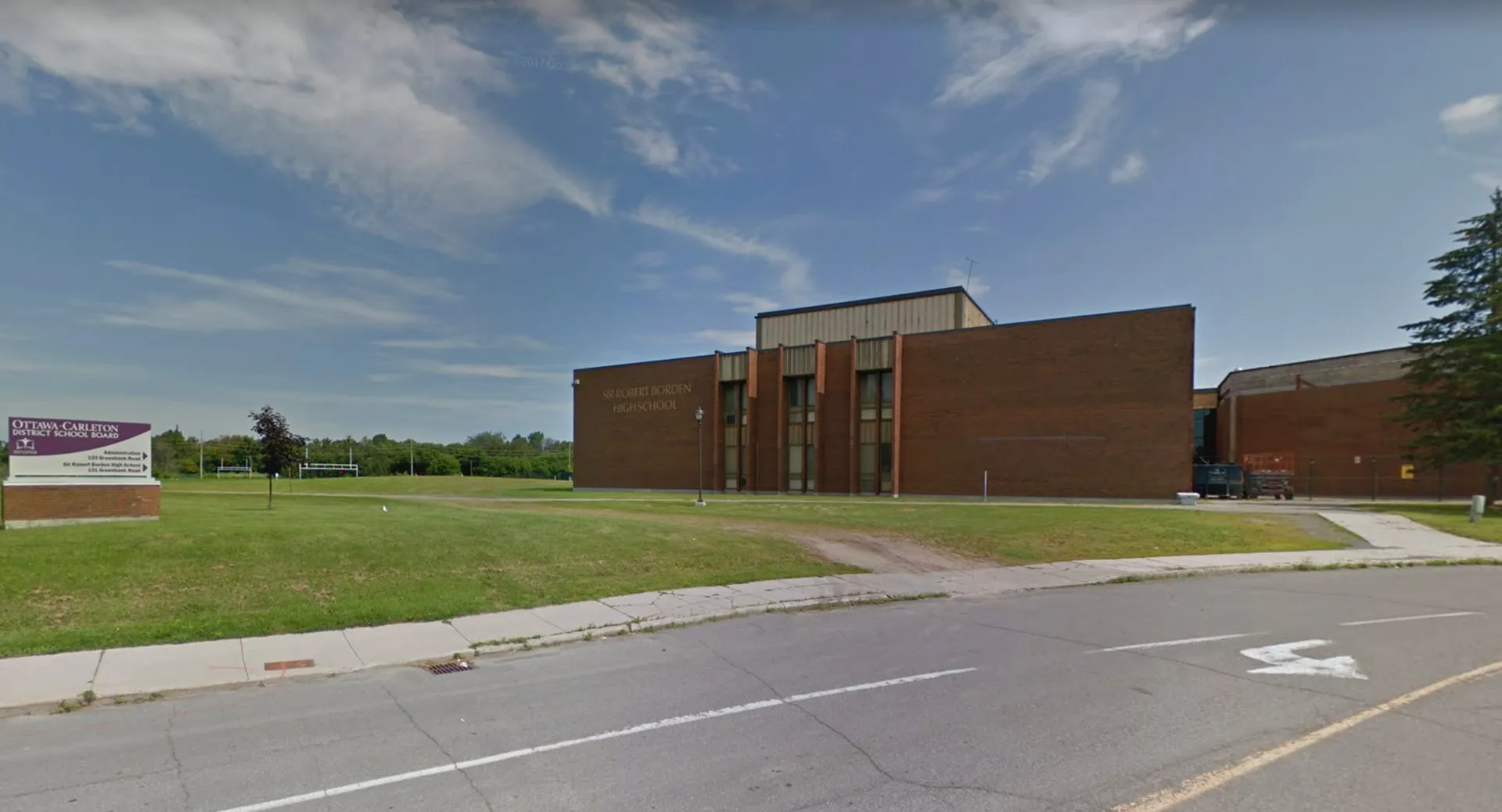 L'edificio in mattoni della Sir Robert Borden High School sorge su un'area verde sotto un cielo azzurro con nuvole.