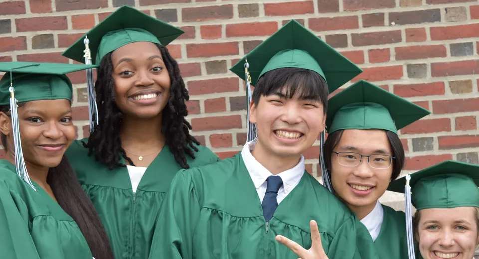 Un gruppo di diplomati del Milford Public School District indossa toghe verdi davanti a un muro di mattoni.