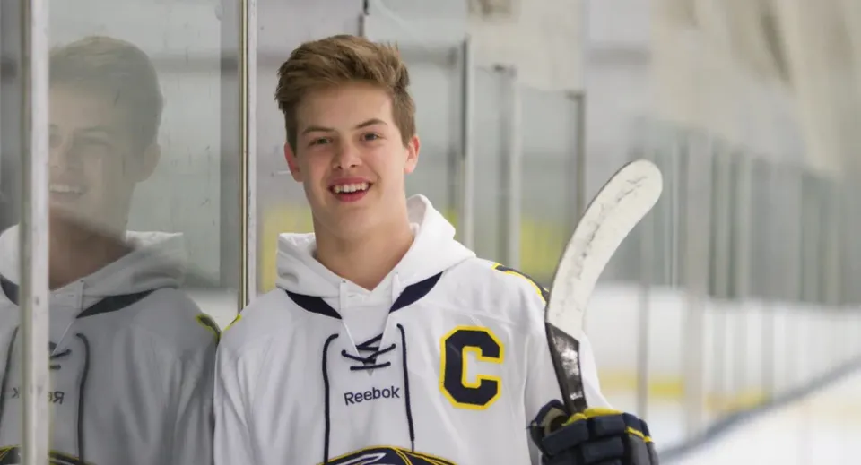Uno studente della Holy Cross High School tiene in mano una mazza da hockey ed è in piedi nel palazzetto del ghiaccio.