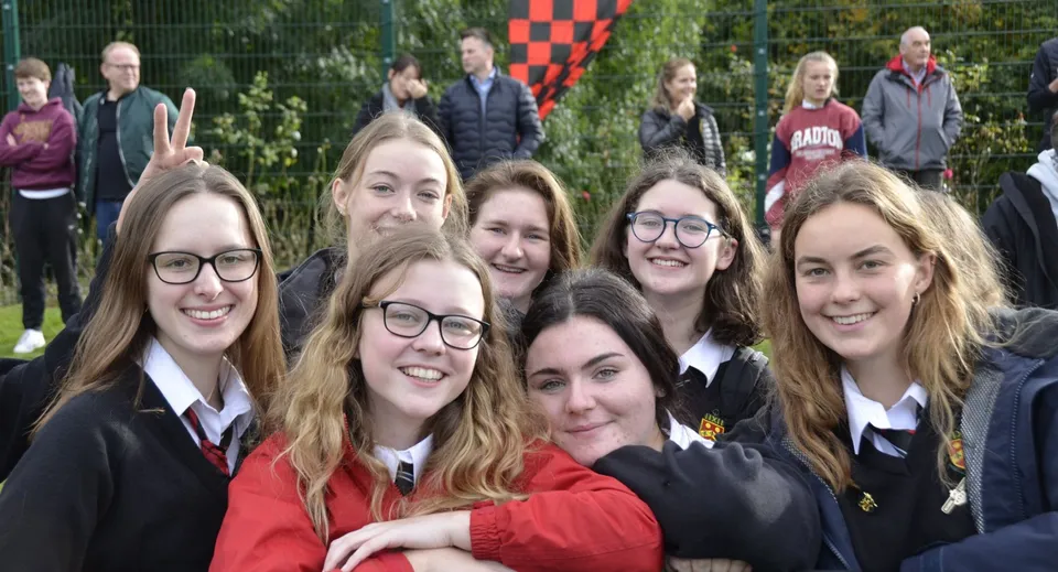 Un gruppo di studentesse della Sutton Park School si trova insieme in un'area verde con alberi e una bandiera a scacchi rossi e bianchi sullo sfondo.