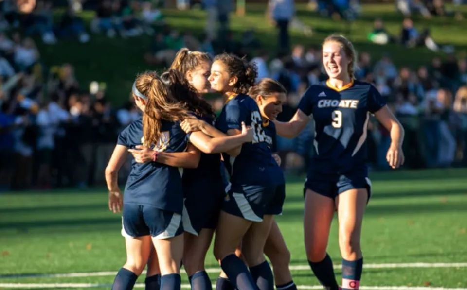 Un gruppo di giovani calciatrici della Choate Rosemary Hall festeggia insieme su un campo in erba davanti agli spettatori.