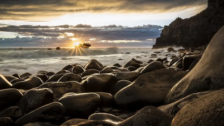 Runde Steine an einer Felsküste bei Sonnenuntergang über dem Meer