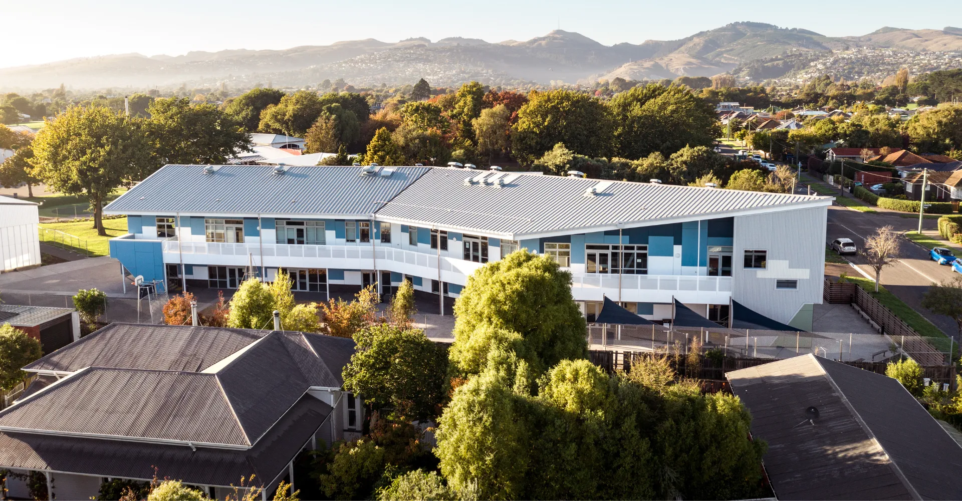 L'edificio moderno a più piani della Hillmorton High School è immerso in un paesaggio verde con le montagne sullo sfondo.