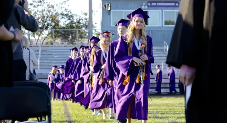 Studenti della Rockford Lutheran School con la toga di laurea viola corrono su un prato davanti a un edificio scolastico.