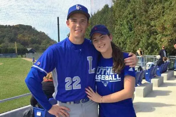 Dos jóvenes sonrientes con gorra y camiseta azul de béisbol en un campo deportivo