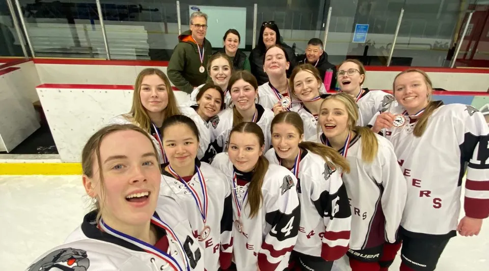 Un gruppo di studentesse della Queen Elizabeth Regional High posa in divisa da hockey su una pista da ghiaccio.