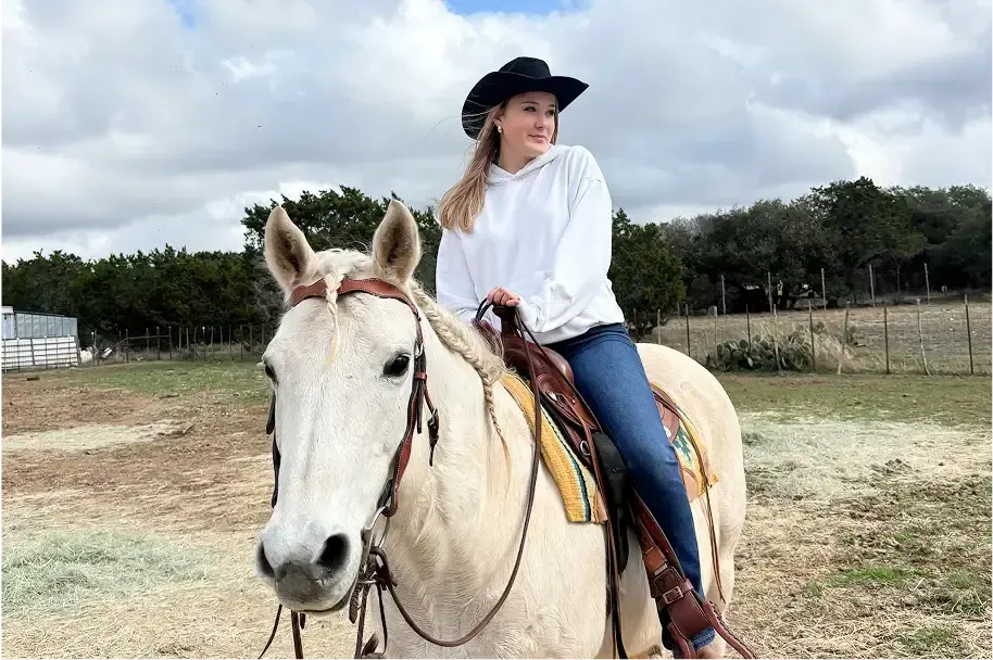Estudiante con sombrero de vaquero montando un caballo blanco en un rancho de Estados Unidos