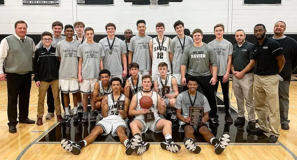 Un gruppo di giocatrici e giocatori di basket della Xavier High School posa con i trofei sul campo da basket.