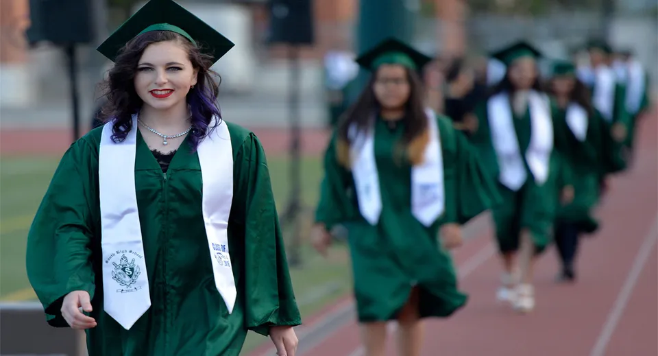 Una diplomata del Torrance Unified School District cammina in toga e tocco verdi su una pista di atletica.