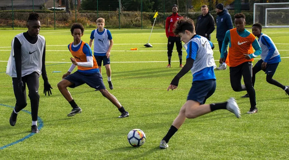Giovani calciatori della Moorland School si allenano con il pallone su un campo in erba sintetica.