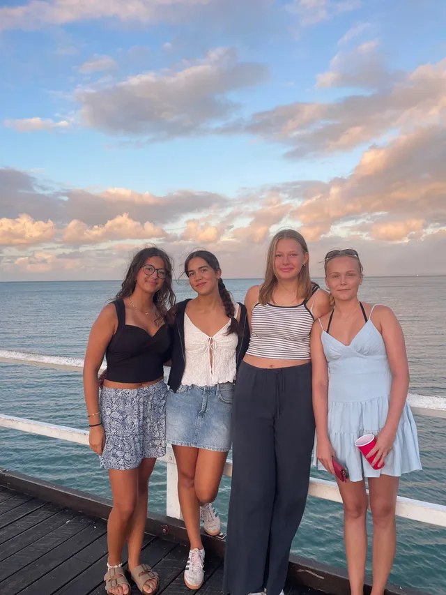 Cuatro chicas posando en un embarcadero de madera junto al mar al atardecer