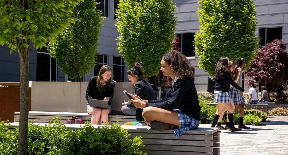 Un gruppo di studenti siede su panchine all'aperto nel terreno della St. Timothy's School.