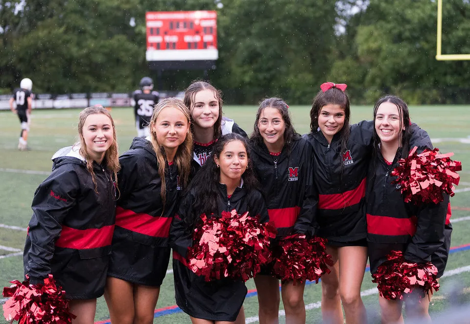 Un gruppo di cheerleader in divisa nera e rossa posa sul campo sportivo della Marblehead High School.
