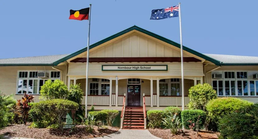 L'edificio scolastico in legno del Nambour State College con veranda e scale, oltre alle bandiere dell'Australia e degli aborigeni.