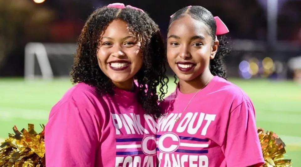 Due studentesse della Norfolk Christian Schools posano insieme con i pompon sul campo sportivo.