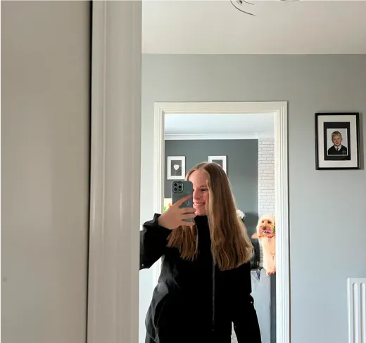 Lorena macht ein Spiegel-Selfie zu Hause, im Hintergrund ein kleiner Hund, in Irland