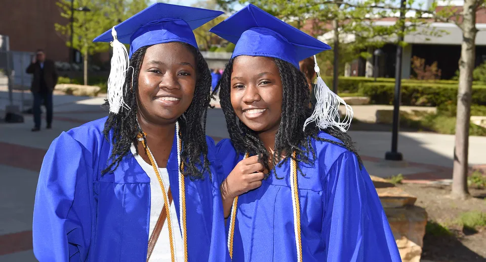 Due studentesse in toga da diploma blu sono insieme davanti a un edificio del campus del Meridan State College.