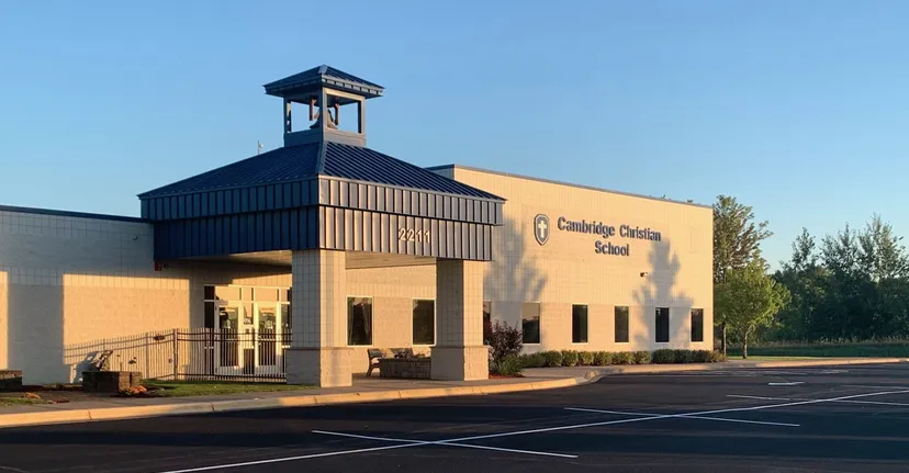 L'edificio scolastico moderno a due piani della Cambridge Christian School, con un ingresso caratteristico e un campanile, è circondato da un parcheggio e da alberi.