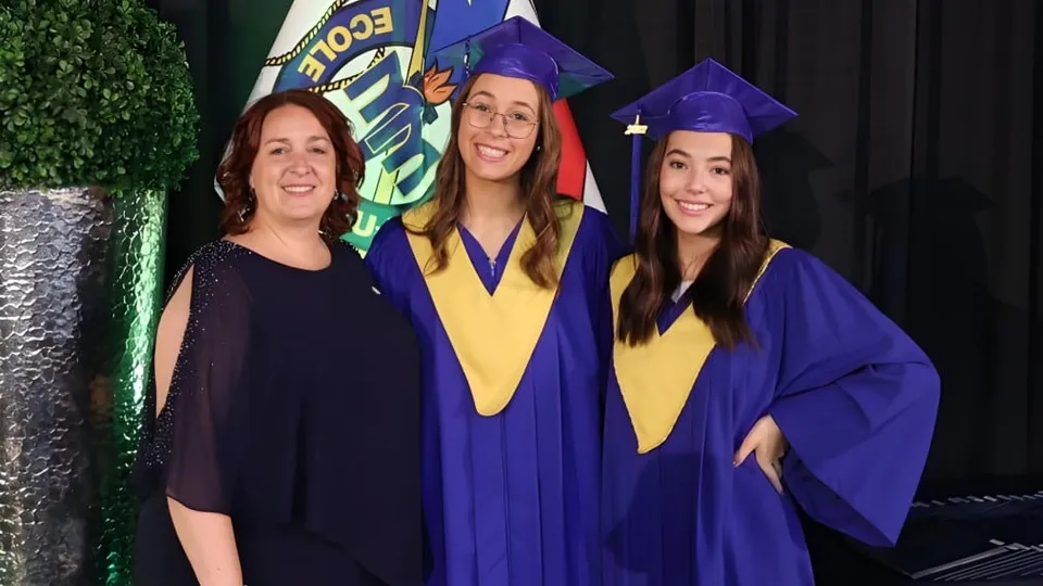 Tre studentesse della École Mathieu-Martin con l'abito da diploma posano davanti a uno sfondo verde con il logo della scuola.