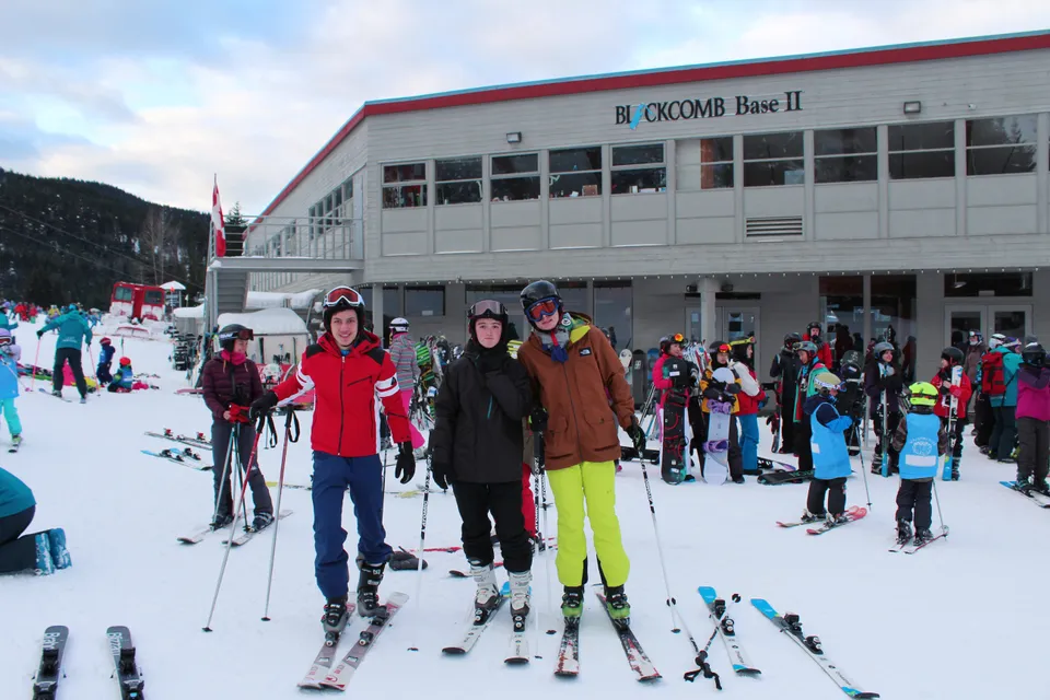 Un gruppo di studenti della Delta Secondary School sta in abbigliamento invernale davanti a uno chalet su una pista da sci innevata.