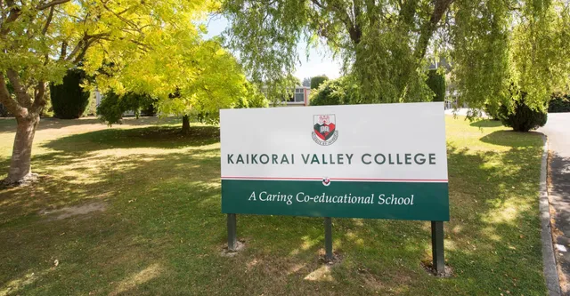 Il cartello del Kaikorai Valley College circondato da alberi con foglie gialle in un ambiente simile a un parco.