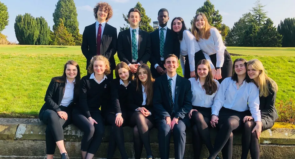 Un gruppo di studenti e studentesse del Stonyhurst College si raccoglie nell'area verde all'aperto tra alberi e prato.