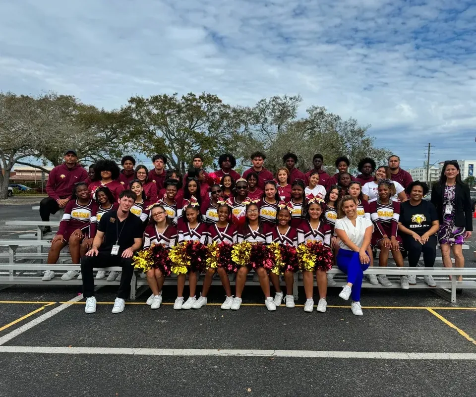Un gruppo di cheerleader in uniforme bordeaux posa insieme sul campo sportivo della Elite Preparatory Academy.