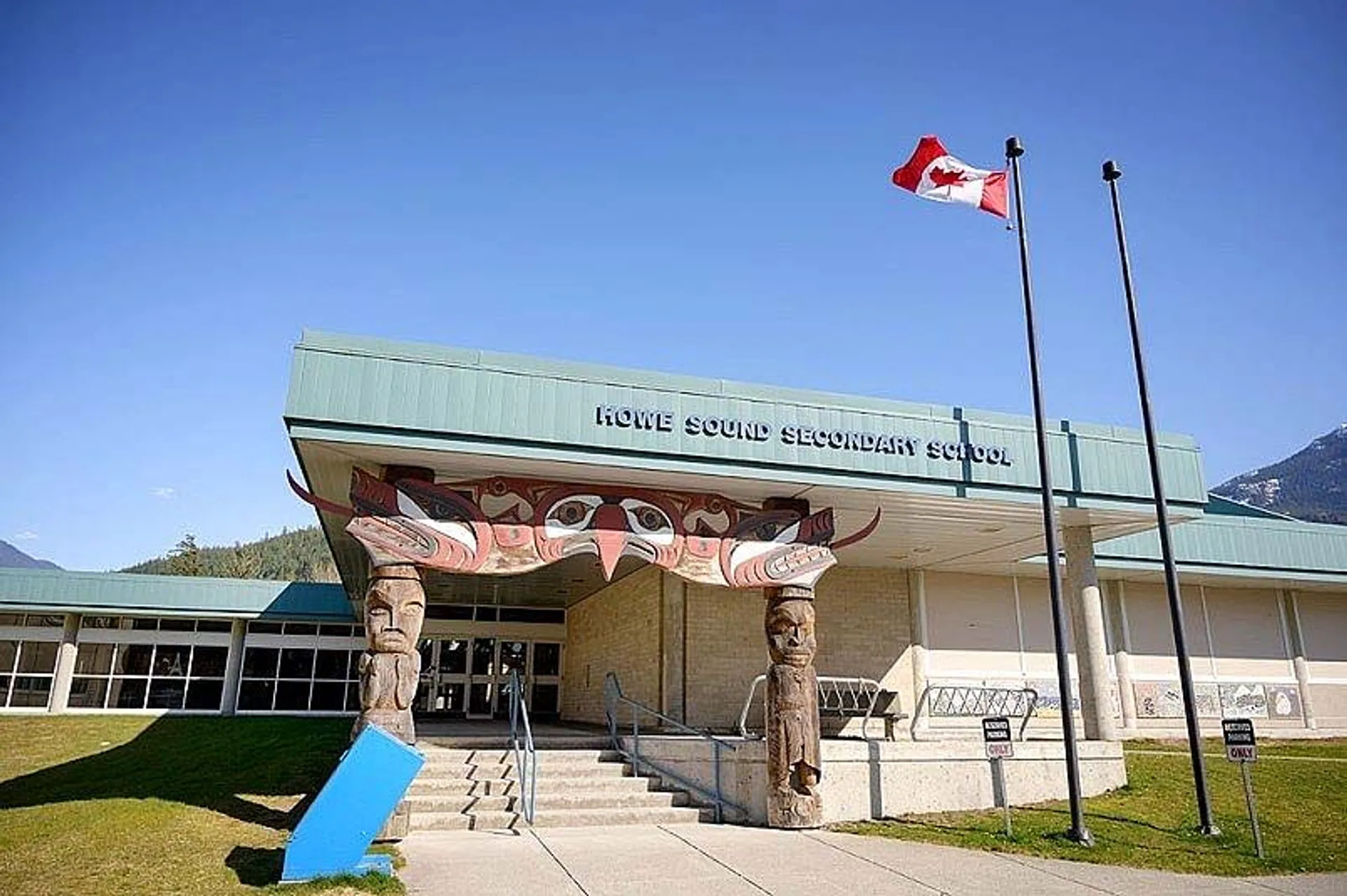 L'edificio moderno della Howe Sound Secondary School con la bandiera canadese, sullo sfondo di montagne e un prato.