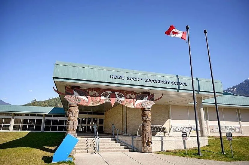 L'edificio moderno della Howe Sound Secondary School con la bandiera canadese, sullo sfondo di montagne e un prato.