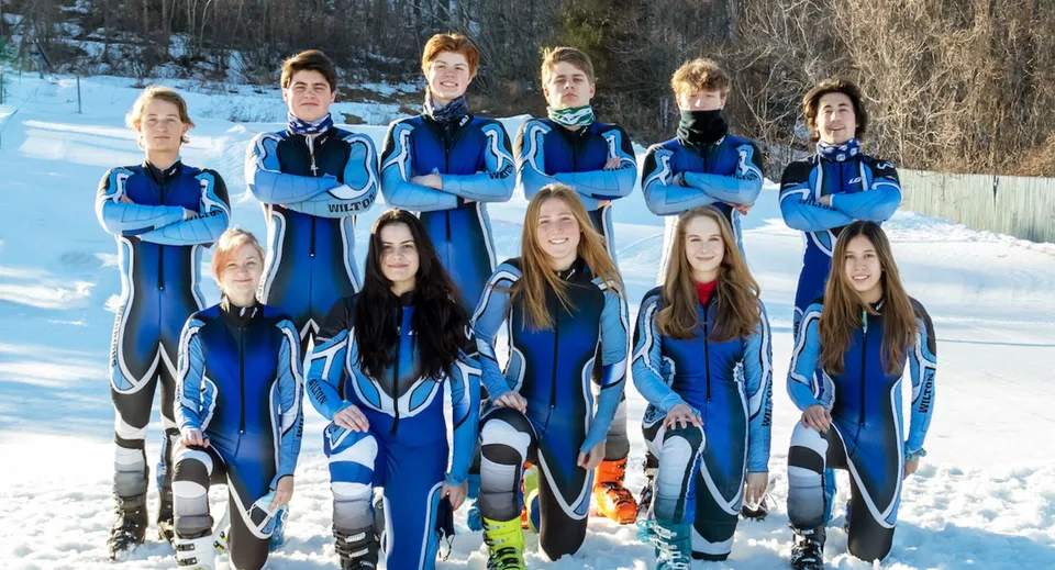 Un gruppo di studenti della Earl of March Secondary School si trova in un bosco innevato indossando tute da sci blu e nere.