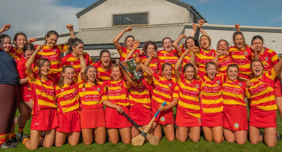 Un gruppo di giovani atlete del Dominican College Galway festeggia insieme su un campo sportivo davanti a un edificio.