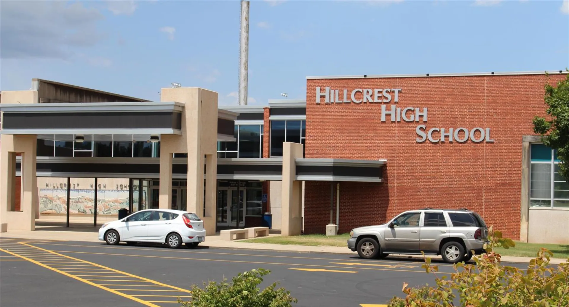 L'edificio in mattoni della Hillcrest High School con il nome sulla facciata e i veicoli parcheggiati davanti.