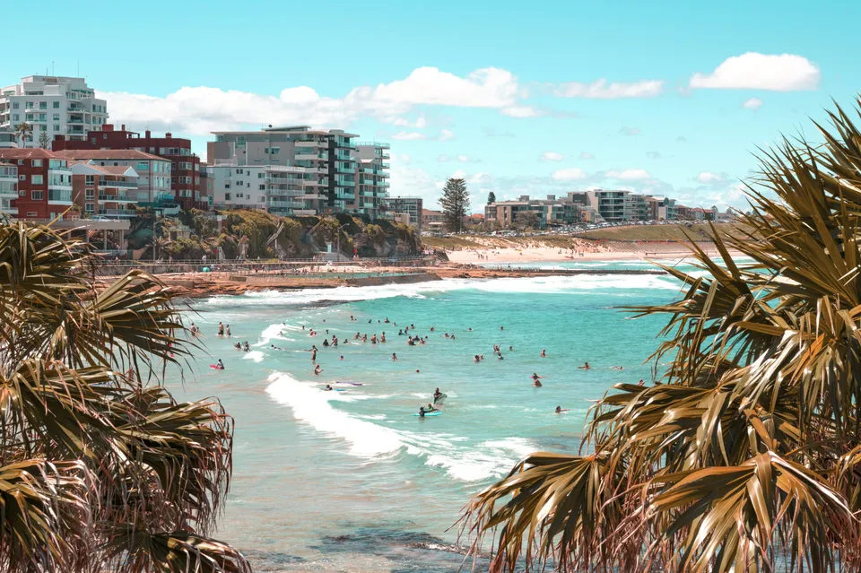 Persone si godono l'acqua limpida e blu sulla spiaggia della Sylvania High School, con grattacieli e palme sullo sfondo.