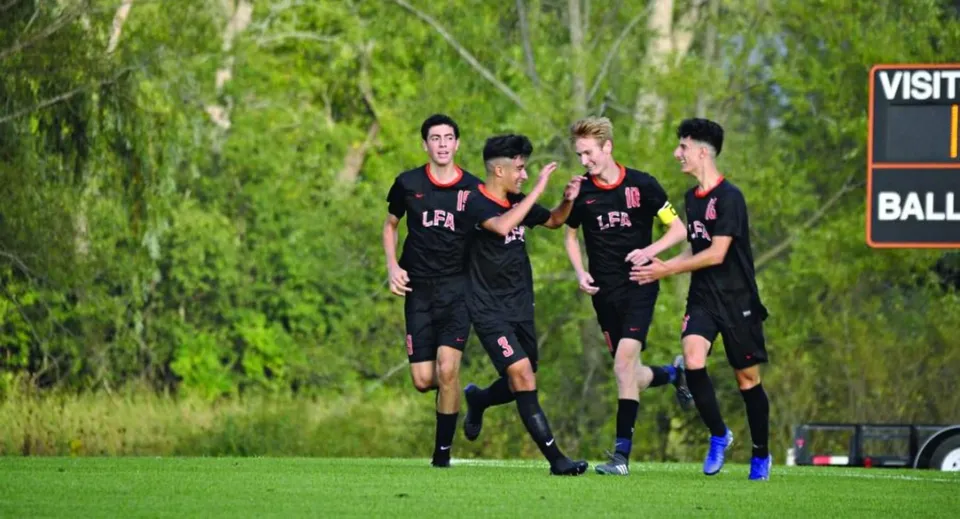 Un gruppo di giovani calciatori in maglia nera corre insieme su un campo verde della Lake Forest Academy.