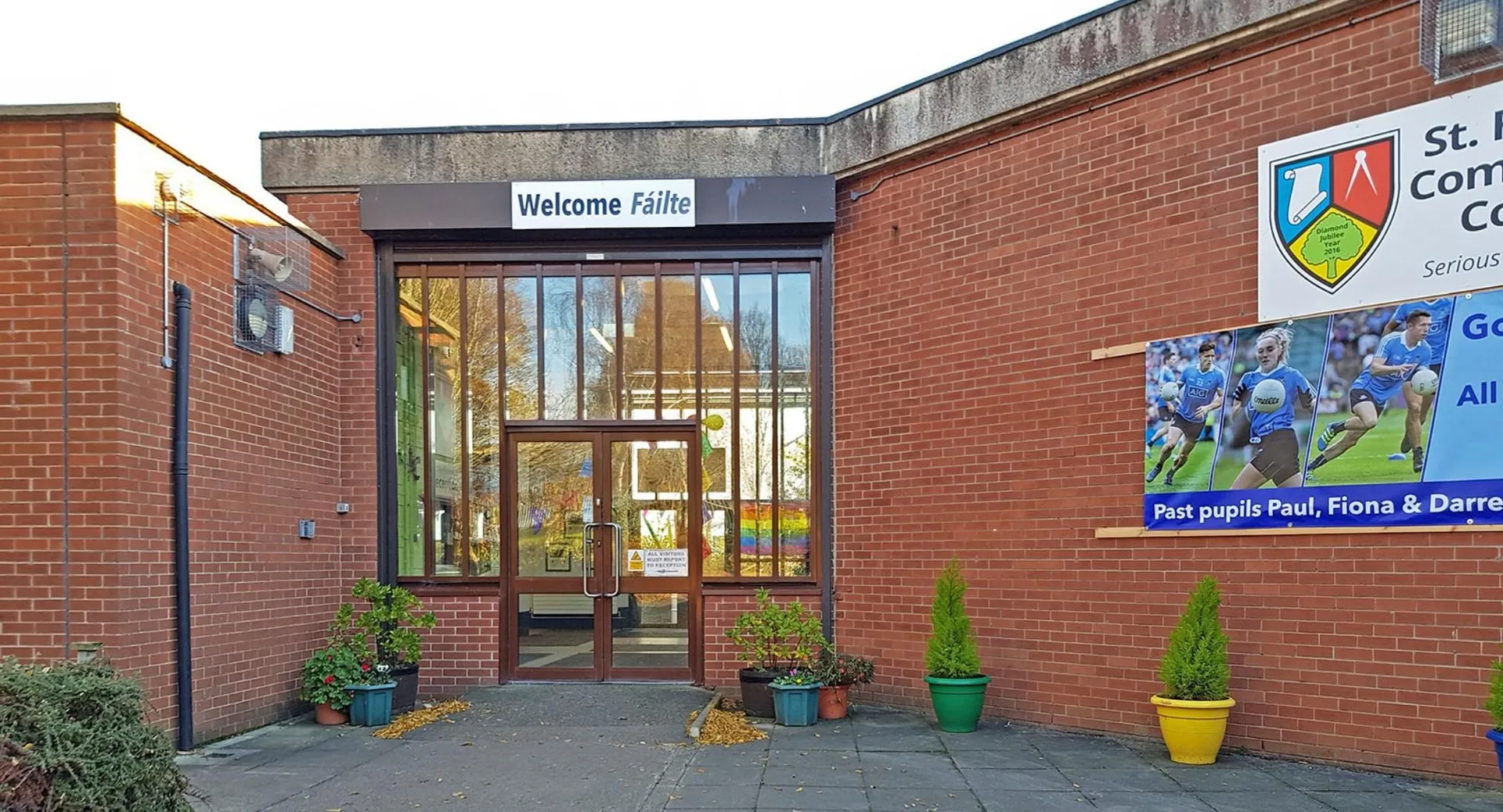 L'area d'ingresso del St. Finian’s Community College con un cartello Welcome Fitness e piante davanti all'edificio in mattoni.