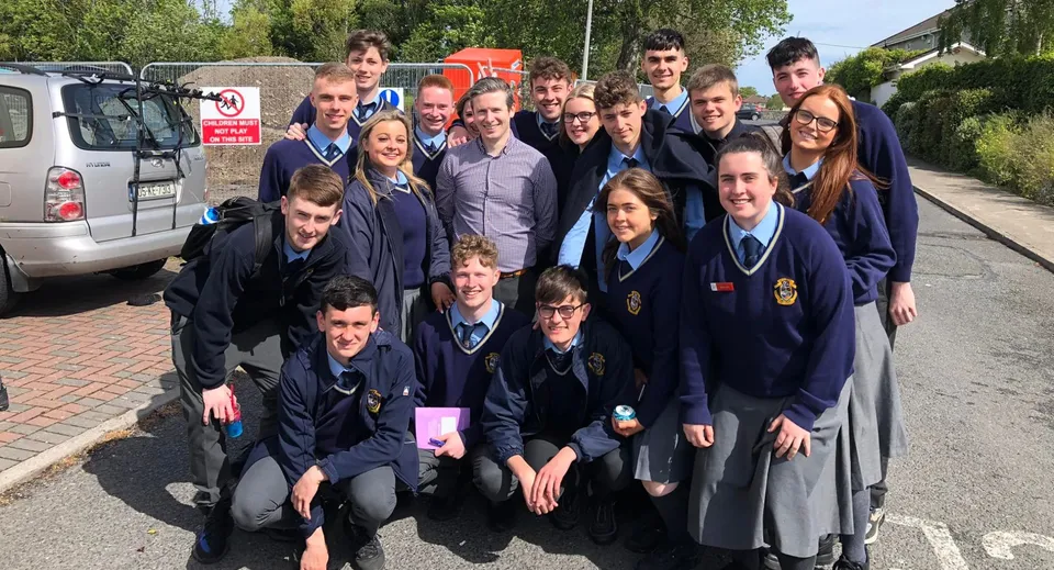 Un gruppo di studenti in divisa scolastica sta in piedi e seduto nell'area esterna della Portmarnock Community School.