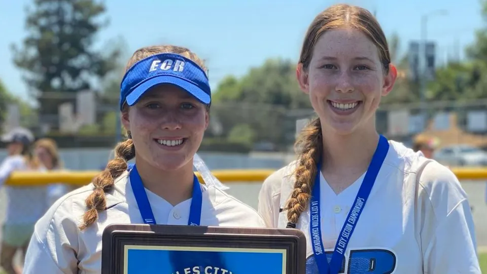 Due studentesse sorridenti della El Camino Real Charter High School sono in piedi davanti a uno specchio d'acqua con alberi ed edifici sullo sfondo.