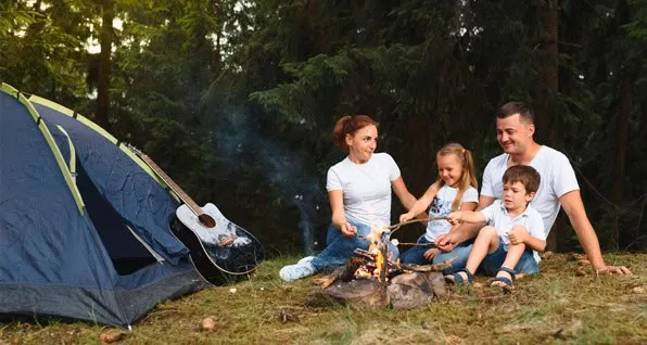 Familia sentada en el bosque junto a una fogata y una tienda de campaña azul