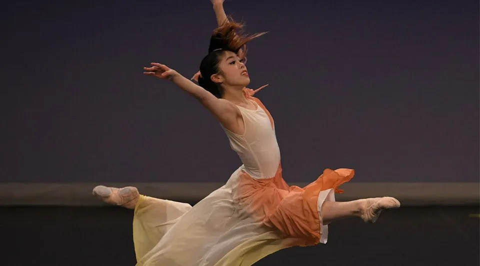 Una ballerina si esibisce sul palco della Moorland School con un vestito bianco e dettagli arancioni.