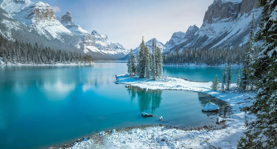 Paesaggio innevato con lago turchese e un'isola boscosa tra le montagne vicino alla Three Hills School.